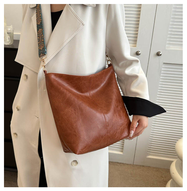 Brown bucket crossbody shoulder bag with wide patterned strap and gold hardware