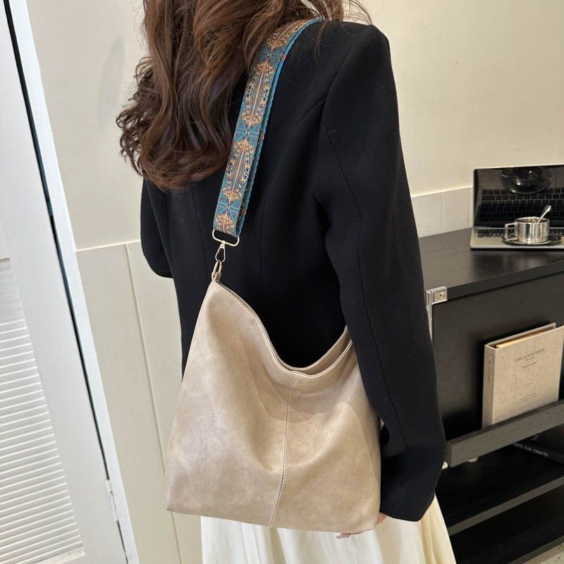 Cream bucket crossbody bag with wide patterned strap and metal clasp handle