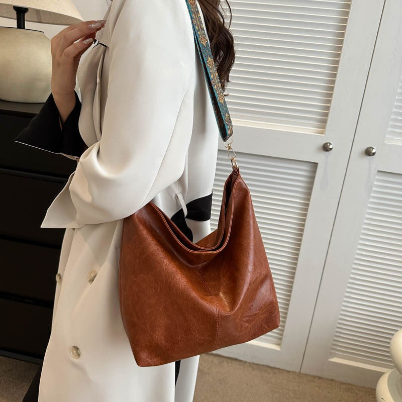 Brown bucket crossbody bag with wide patterned shoulder strap