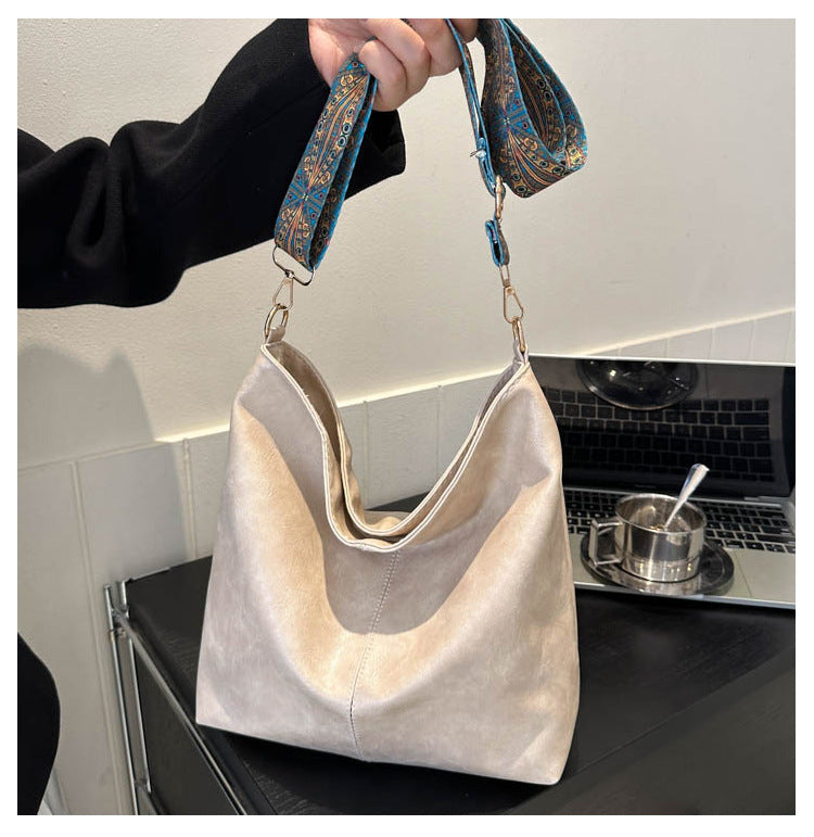 Cream bucket crossbody bag with wide patterned strap and metal clasp handles