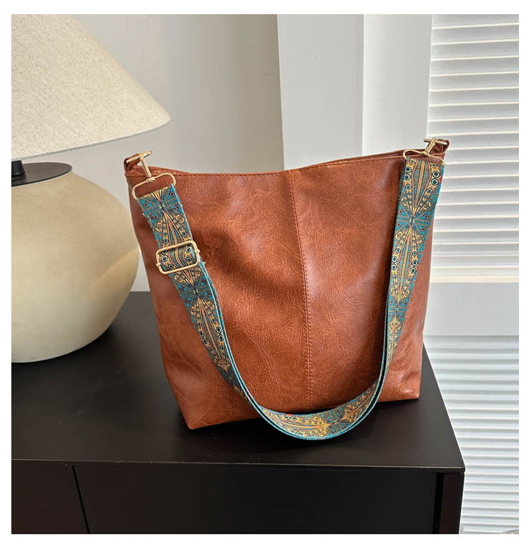 Rust brown bucket crossbody bag with turquoise patterned wide strap