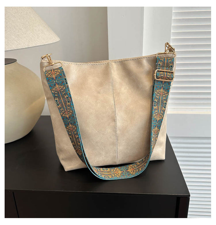Cream bucket crossbody bag with turquoise patterned wide shoulder strap and gold hardware