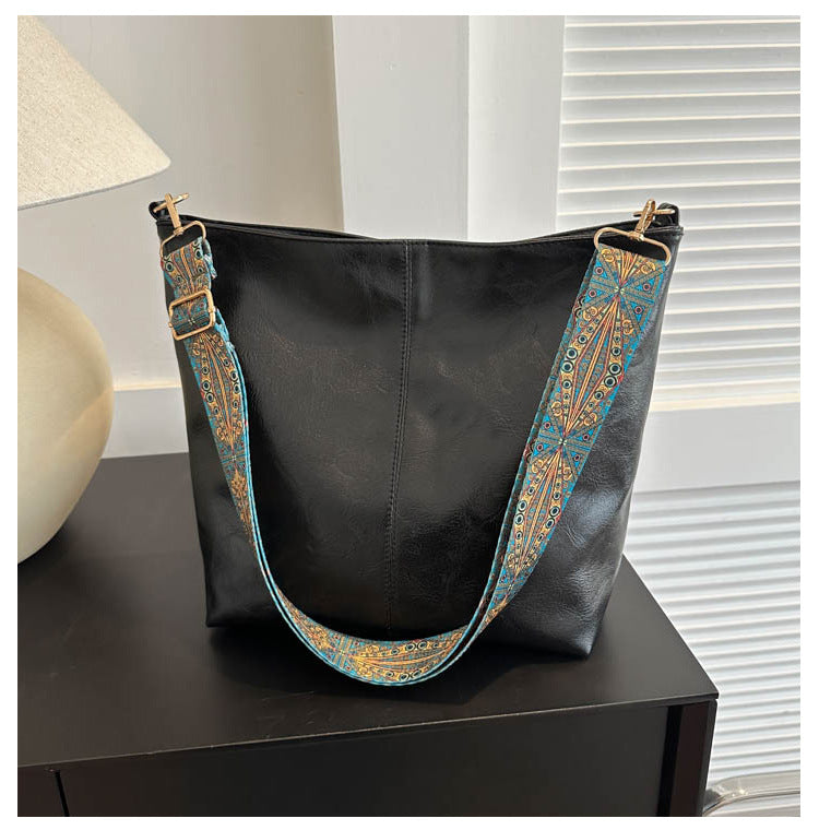 Black bucket crossbody bag with turquoise patterned wide strap